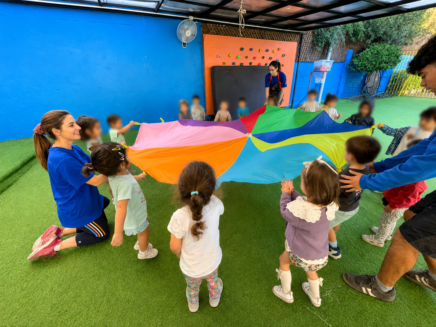 Niños y educadoras jugando con paracaídas de colores al aire libre